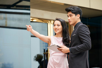 Asian businesswoman pointing at something showing that thing to young man standing next to her