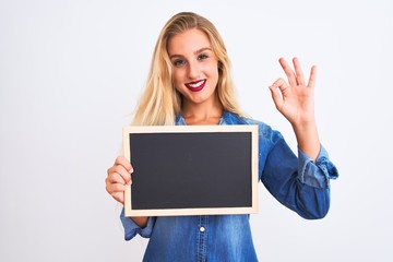 Naklejka premium Young beautiful teacher woman holding blackboard standing over isolated white background doing ok sign with fingers, excellent symbol