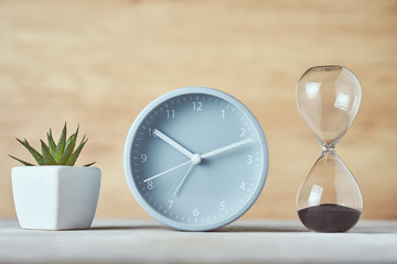Fototapeta na wymiar Hourglass, alarm clock and plant on the table, close up