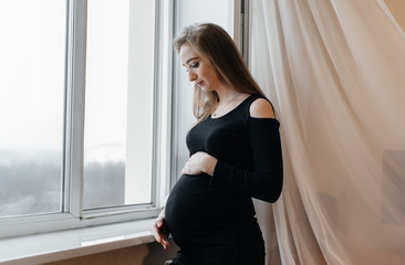 A pregnant girl is breathing fresh air from the window