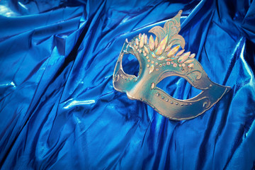 Photo of elegant and delicate Venetian mask over blue silk background