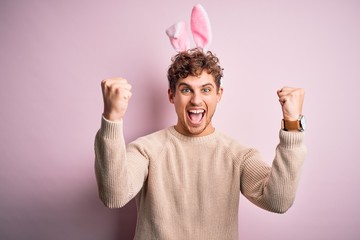 Young handsome blond man wearing easter rabbit ears over isolated pink background celebrating surprised and amazed for success with arms raised and open eyes. Winner concept.
