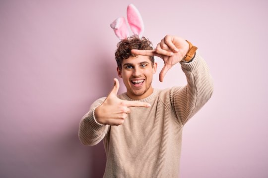 Young handsome blond man wearing easter rabbit ears over isolated pink background smiling making frame with hands and fingers with happy face. Creativity and photography concept.