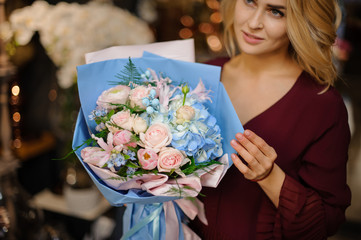 Girl holding a spring bouquet of blue hydrangeas and creamy roses wrap in paper with green leaves