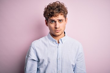 Young blond handsome man with curly hair wearing striped shirt over white background skeptic and nervous, frowning upset because of problem. Negative person.