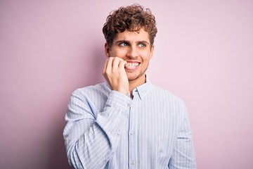 Fototapeta na wymiar Young blond handsome man with curly hair wearing striped shirt over white background looking stressed and nervous with hands on mouth biting nails. Anxiety problem.