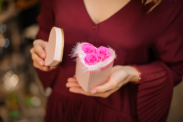 Woman holding a little heart shape box full of white feathers and pink roses