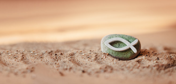 Kommunion, Konfirmation, Firmung, Taufe - weißer Fisch aus Holz auf grün bemalten Stein im Sand