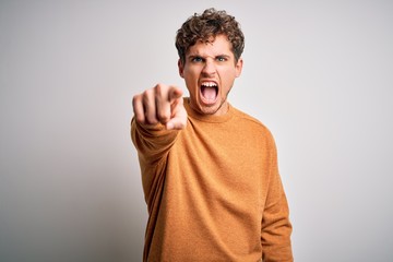 Young blond handsome man with curly hair wearing casual sweater over white background pointing displeased and frustrated to the camera, angry and furious with you