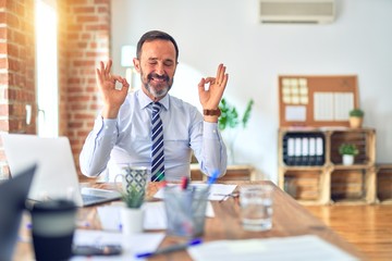 Middle age handsome businessman wearing tie sitting using laptop at the office relax and smiling with eyes closed doing meditation gesture with fingers. Yoga concept.