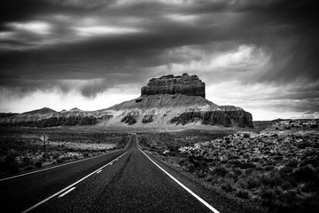 A long straight road through the Utah desert with Storm coming upon a mountain, near Goblin Valley...