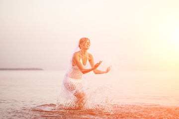 Bride on beach at sunset. Beautiful woman in white wedding dress with bouquet. Wedding by sea. A romantic trip to  tropical island in ocean. Happy girl