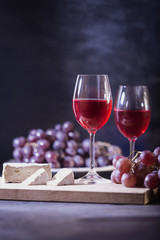 A glass of red fruit wine. Close-up of grape vine and brie cheese on a dark blue background in low key. Copy space. Banner for cafe, winery and restaurant.