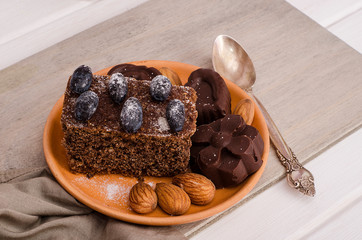 Chocolate cake, muffin with chocolate candies, decorated with berries, icing sugar and almonds on a clay saucer on a white wooden background.