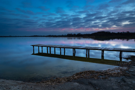 A long wooden bridge towards the water, evening blue and pink clouds after sunset in Staw, Poland