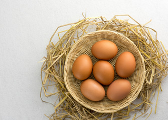 Brown chicken eggs in a basket on a separate straw on a white background.