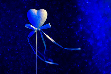 A heart with a bow. Blue blurred bokeh in the background. The concept for Valentine's Day