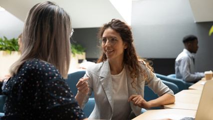 Obraz na płótnie Canvas Millennial female employees talk sharing ideas at workplace