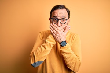 Middle age hoary man wearing casual sweater and glasses over isolated yellow background shocked covering mouth with hands for mistake. Secret concept.
