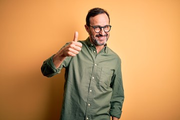 Middle age hoary man wearing casual green shirt and glasses over isolated yellow background doing...