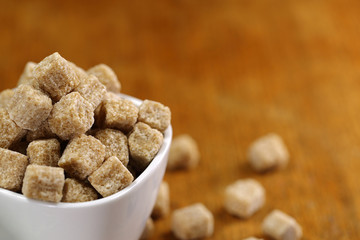 cup full of pieces of white and brown sugar on a wooden table with a blurred background