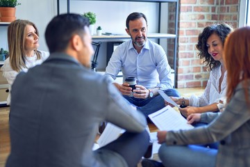 Group of business workers smiling happy and confident. Sitting on the floor relaxed working together speaking and reading documents at the office