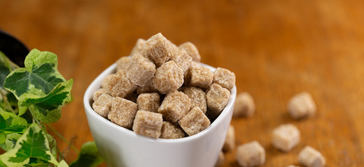 cup full of pieces of white and brown sugar on a wooden table with a blurred background