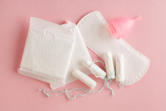 menstruation cycle, feminine hygiene and protection products, sanitary pads, tampons and menstrual cup on pastel pink background, top view, flat layout
