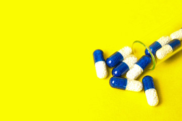 Medicine blue with white capsules (pills) in the test tube on yellow background. Copy space. Medical background, template.
