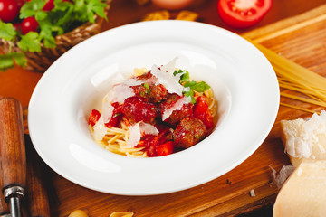 Italian pasta. Spaghetti with tomato sauce and meatballs on white plate with parmesan cheese, fresh parsley and tomatoes on rustic wooden background.