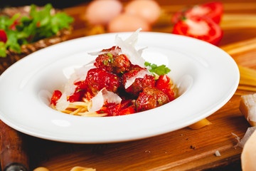 Italian pasta. Spaghetti with tomato sauce and meatballs on white plate with parmesan cheese, fresh parsley and tomatoes on rustic wooden background.