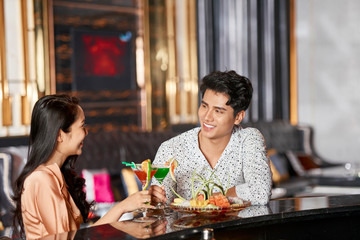 Romantic couple spending evening together in modern spa resort hotel saloon drinking liquor cocktails