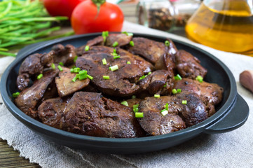 Fried chicken liver with young green onions in a cast-iron frying pan on a wooden background. Tasty healthy dish