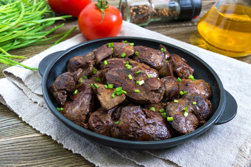 Fried chicken liver with young green onions in a cast-iron frying pan on a wooden background. Tasty healthy dish