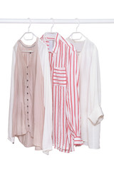 Hanging blouses isolated. Closeup of collection of three female various colorful blouses on a clothes rail isolated on a white background. Womens summer fashion.