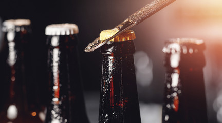 Glass ice cold bottles of beer with opener cap on dark background