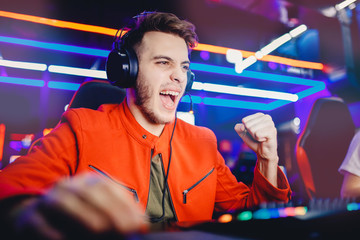 Streamer young man rejoices in victory professional gamer playing online games computer with headphones, neon color
