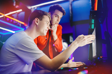 Team of two guys playing online video games analyzes strategy of fighting behind computer monitor...