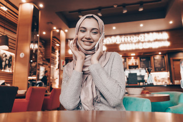 Muslim woman sitting at a cafe table smiling tenderly and propping her cheek with her hand
