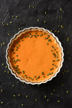 Healthy dessert concept. Open pumpking pie with seeds in white baking dish on black background copy space