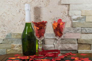 Paper hearts, red tape on the two glasses of champagne, bottle on the stone background.