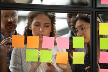 Focused multiethnic colleagues write on colorful sticky notes