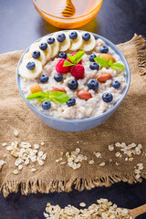 Oatmeal porridge with berries, fruits and honey on dark background. Oatmeal with raspberries, blueberries and almonds on burlap. Healthy breakfast