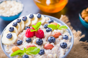 Oatmeal porridge with berries, fruits and honey on dark background. Oatmeal with raspberries, blueberries and almonds on burlap. Healthy breakfast