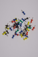 Thumbtacks of different bright colors are scattered randomly on a gray background.