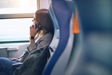 Young beautiful woman smiling happy and confident. Sitting with smile on face talking by smartphone travelling by train