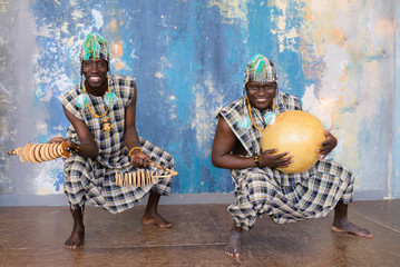 African artists with traditional musical instruments on blue wall background.