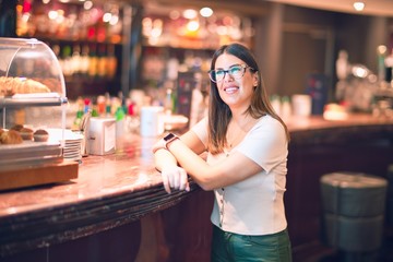 Young beautiful woman smiling happy and confident. Standing with smile on face leaning on the counter bar at restaurant