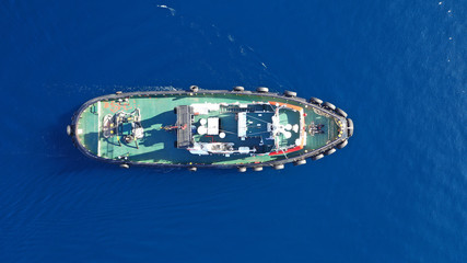 Aerial drone top down photo of tug boat cruising in industrial carrier logistics terminal
