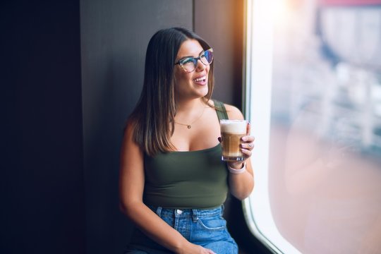 Young beautiful woman on vacation smiling happy and confident. Standing on a deck of ship with smile on drinking coffee face doing a cruise